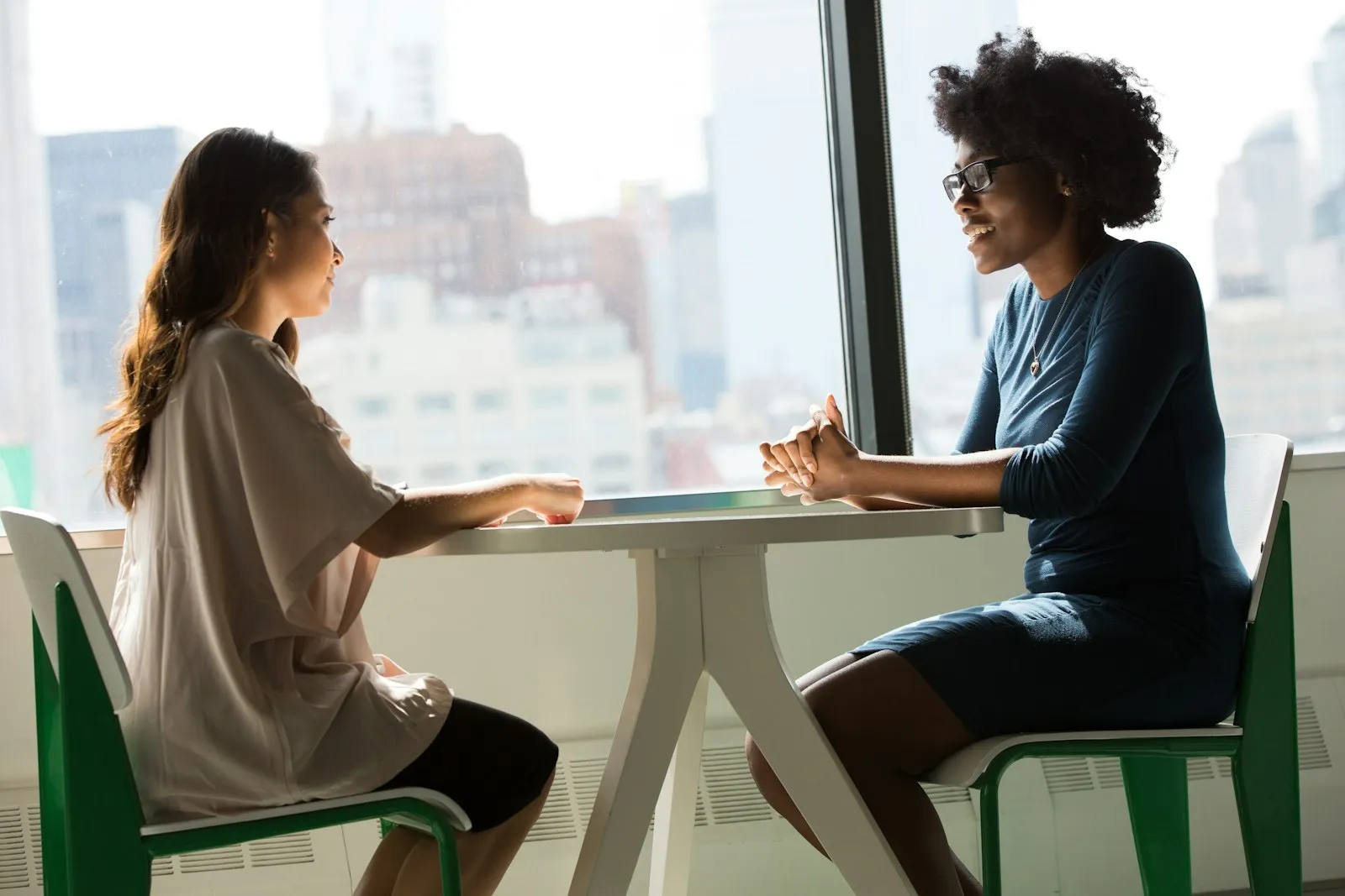 Two people talking across a small table by a bright window